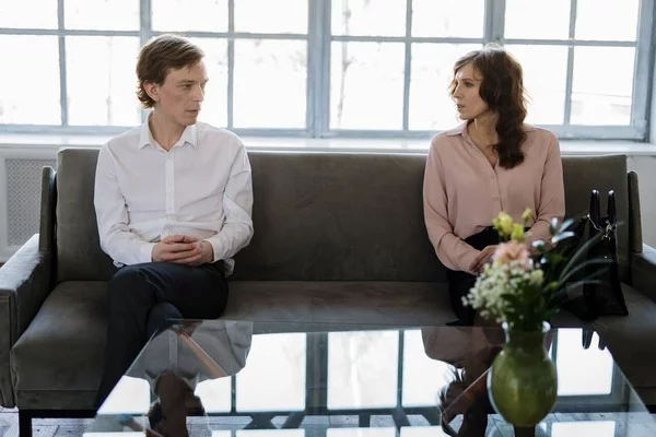 kobieta i mężczyzna siedzący po dwóch stronach sofy w separacji, przed nimi szklany stolik z wazonem z kwiatkami - rozwód z orzeczeniem o winie