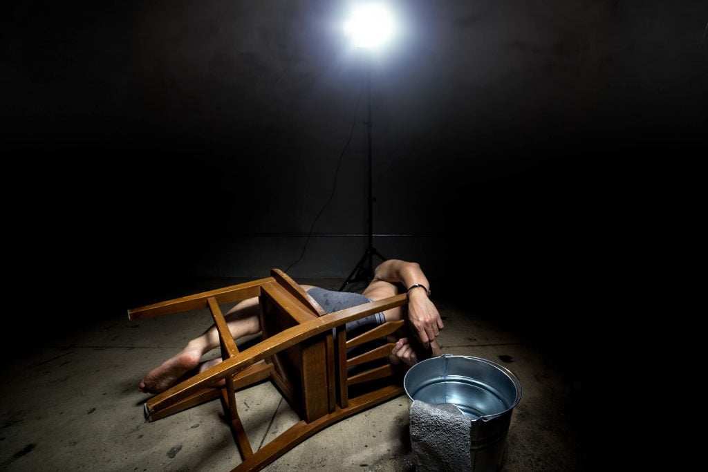 osoba przywiązana do krzesła leży na betonowej posadzce, obok stoi lampa i wiadro z wodą - odszkodowania za represje stalinowskie