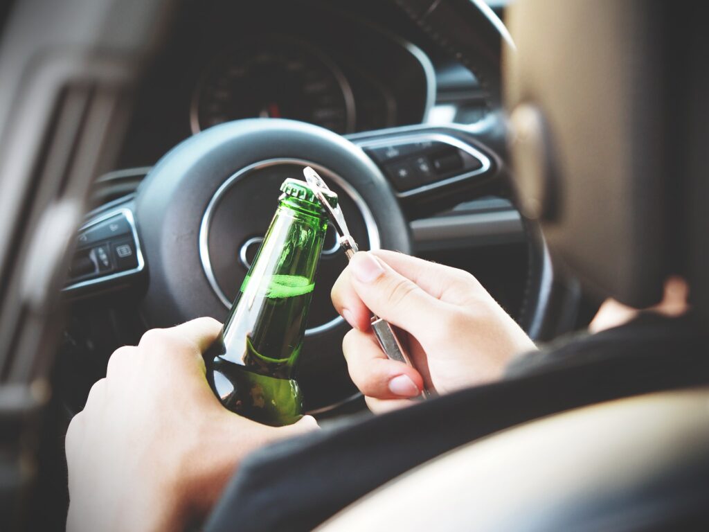 Konfiskata samochodu za alkohol - osoba siedząca na miejscu kierowcy w samochodzie otwiera piwo w butelce